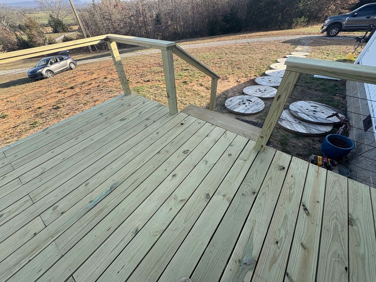 Wooden backyard deck with railings overlooking a yard and several round concrete pads below.