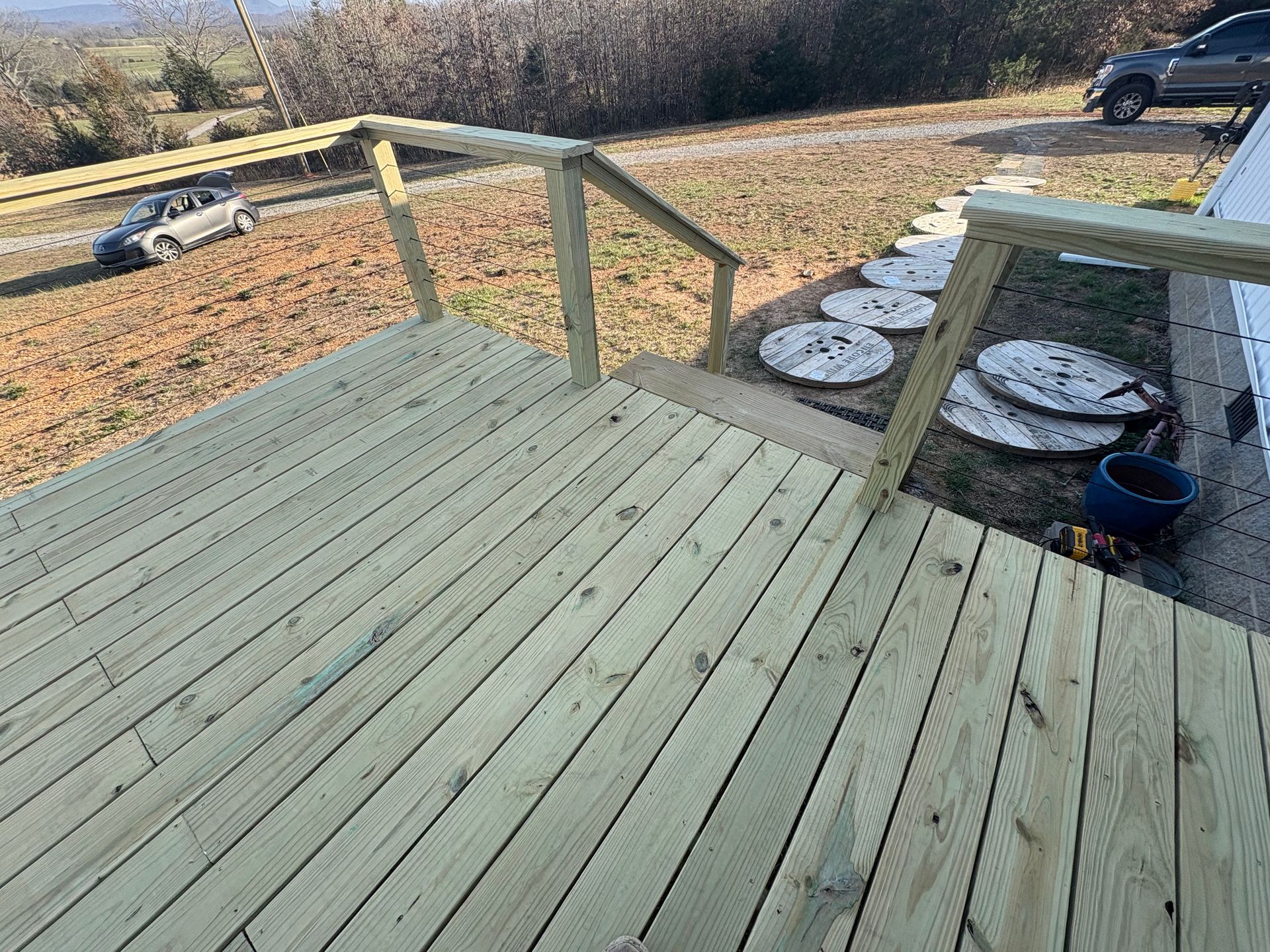 Newly built wooden deck with railing and steps leading to a yard with a car on the road.