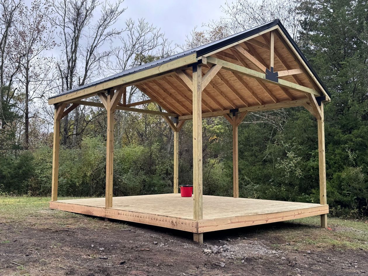 Wooden pavilion with a raised platform and pitched roof in a wooded outdoor setting
