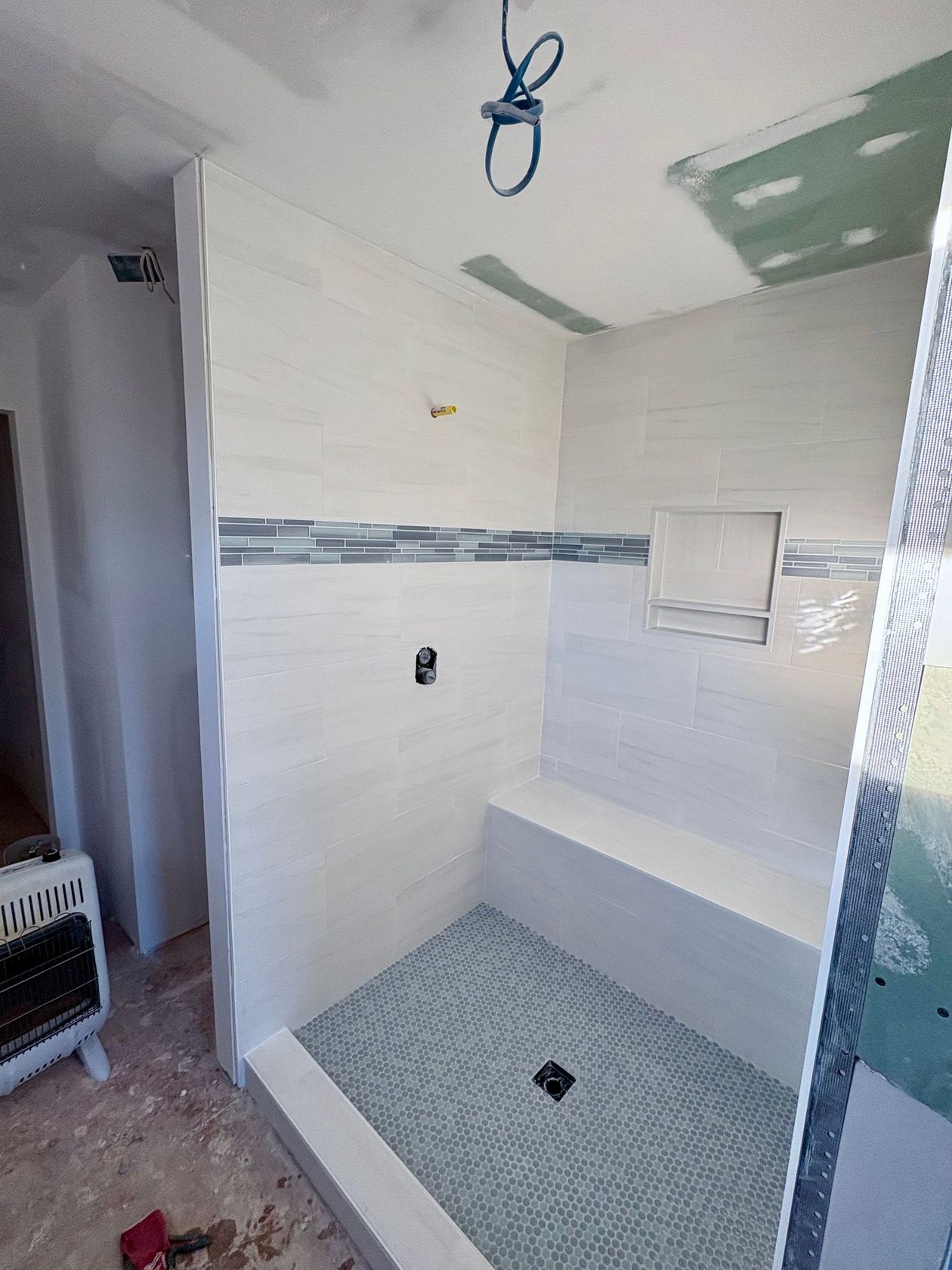 Partially tiled bathroom shower under renovation, with exposed fixtures and a blue mosaic floor base.