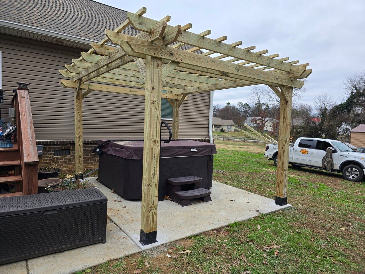 A hot tub is under a wooden pergola in the backyard of a house.