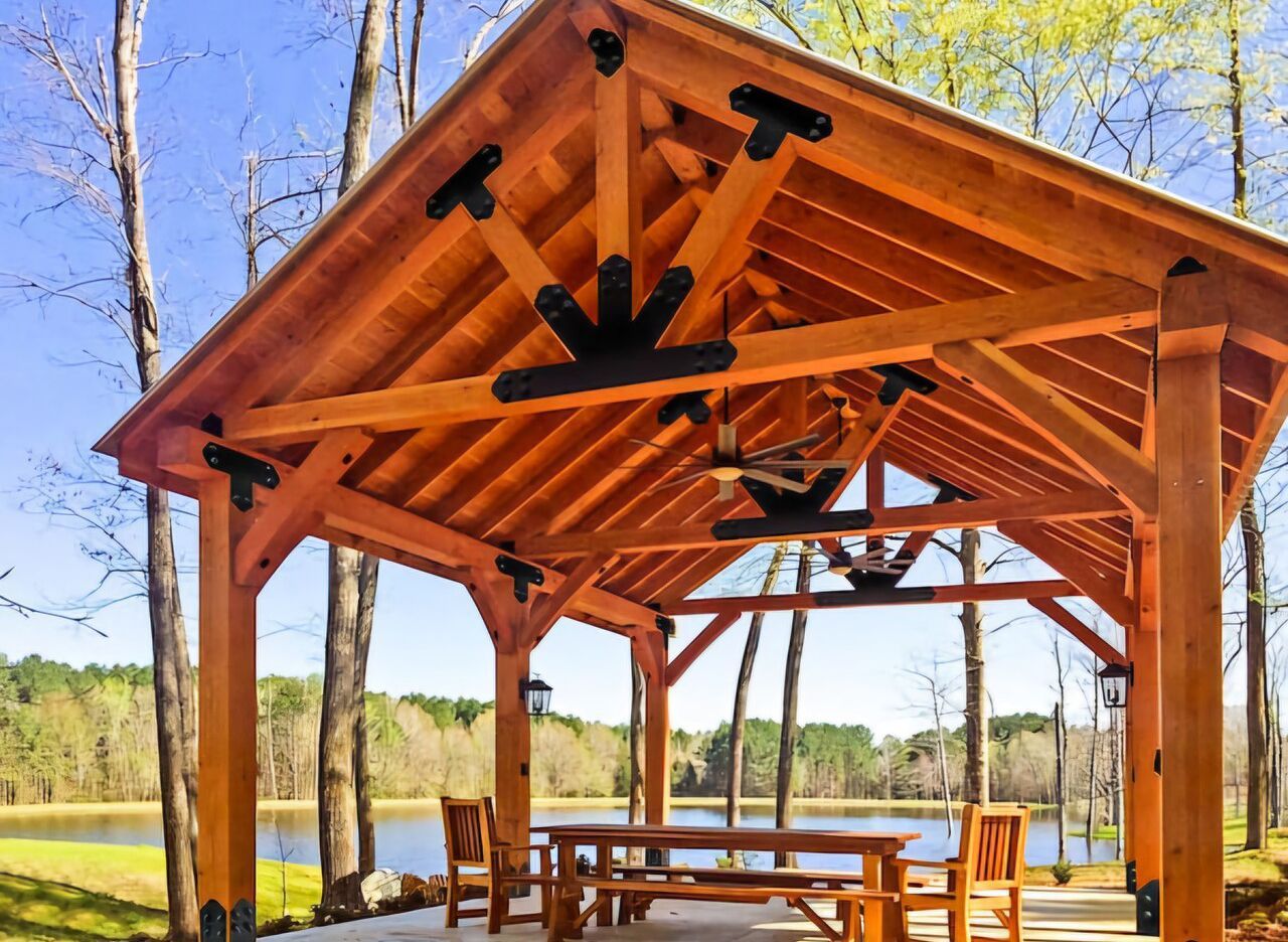 A wooden pavilion with a table and chairs in front of a lake