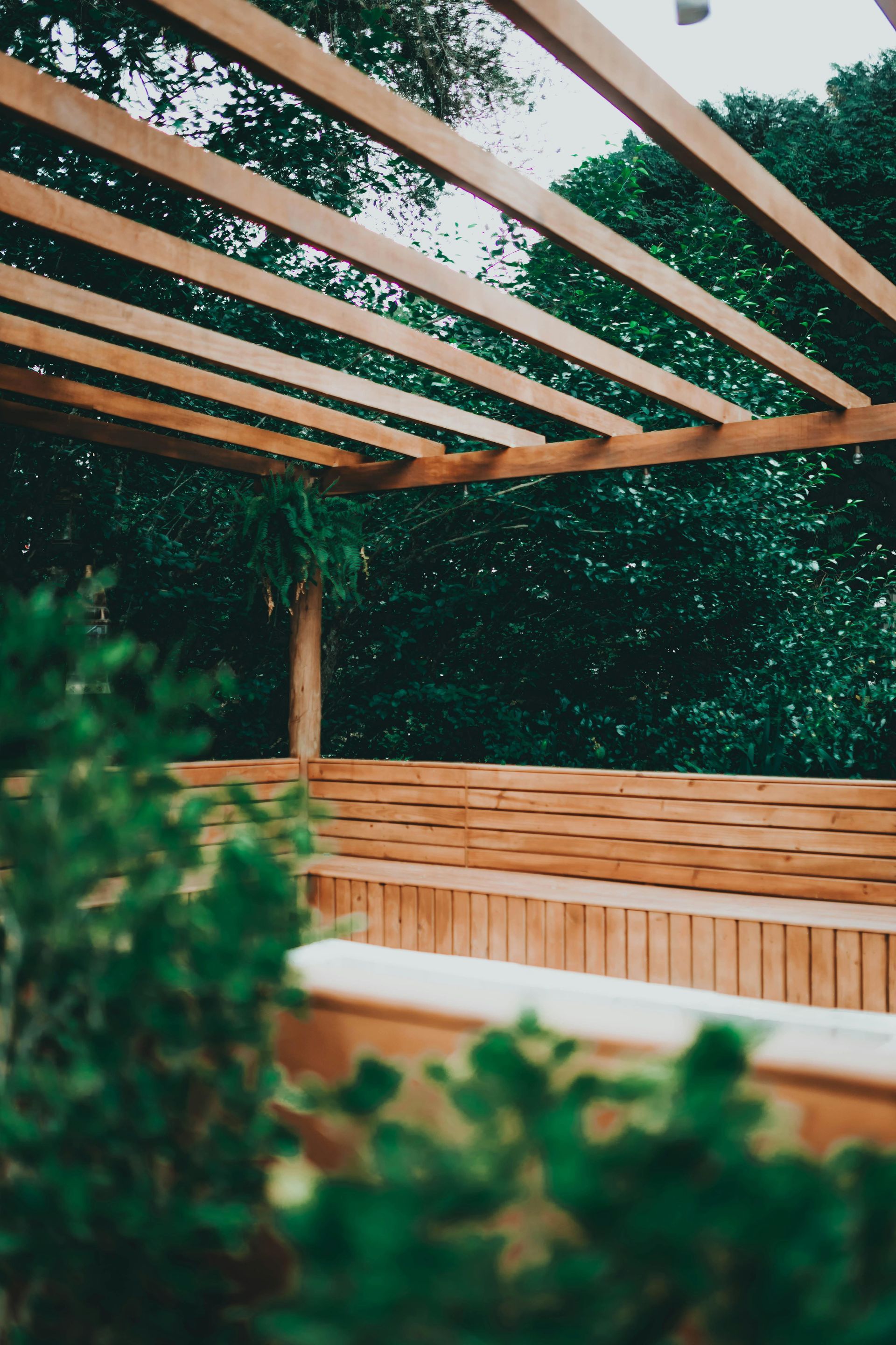 Wooden pergola with seating area overlooking lush green trees.