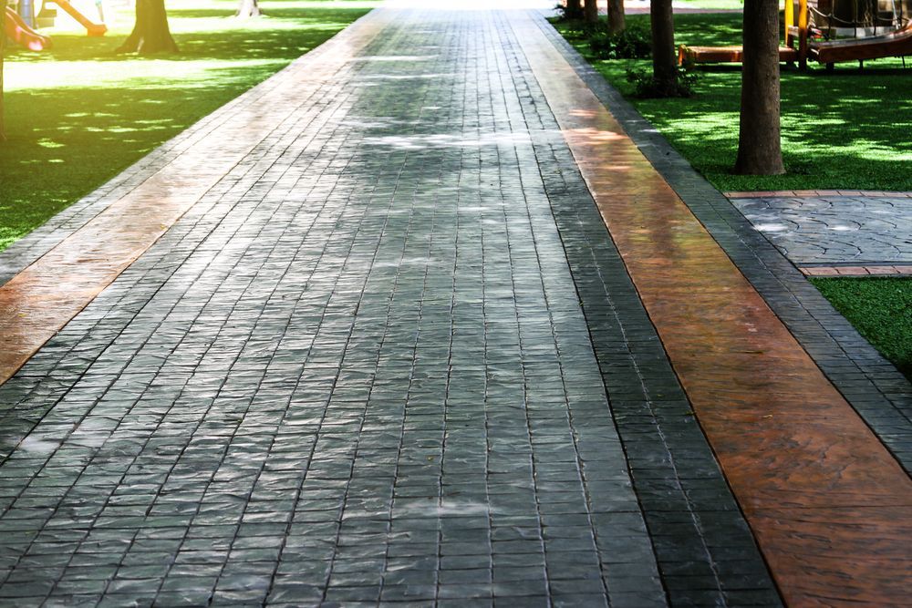 Brick-patterned concrete pathway with an orange-brown border, lined with grass and trees.