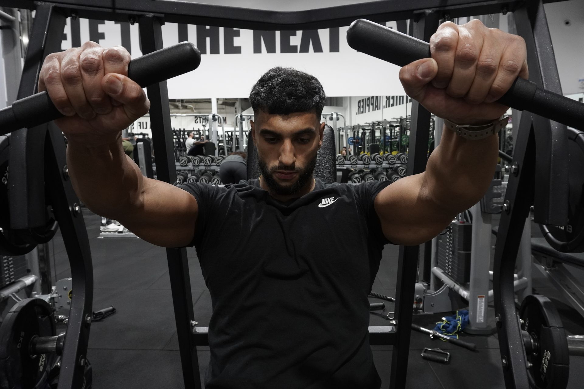 Manni kumar  i is using a machine in a gym with a sign that says fit the next