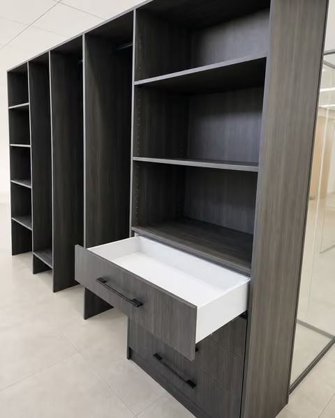 Dark wood built-in shelves and cabinets with open compartments and a white pull-out drawer in a showroom.