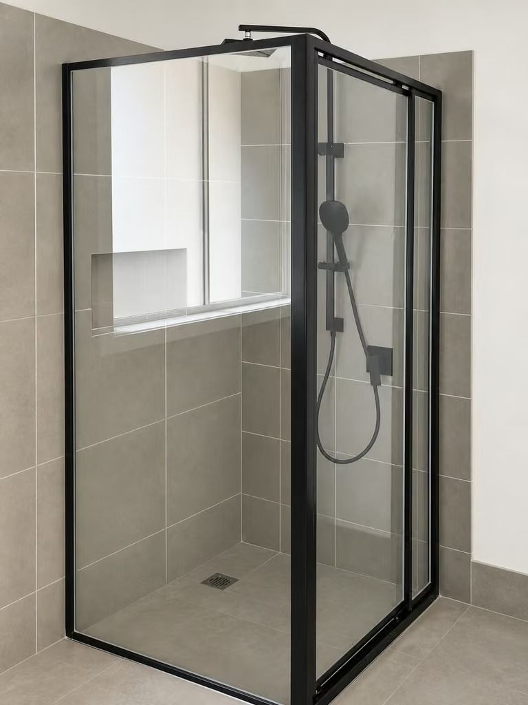 Modern tiled shower with black-framed glass enclosure and handheld showerhead