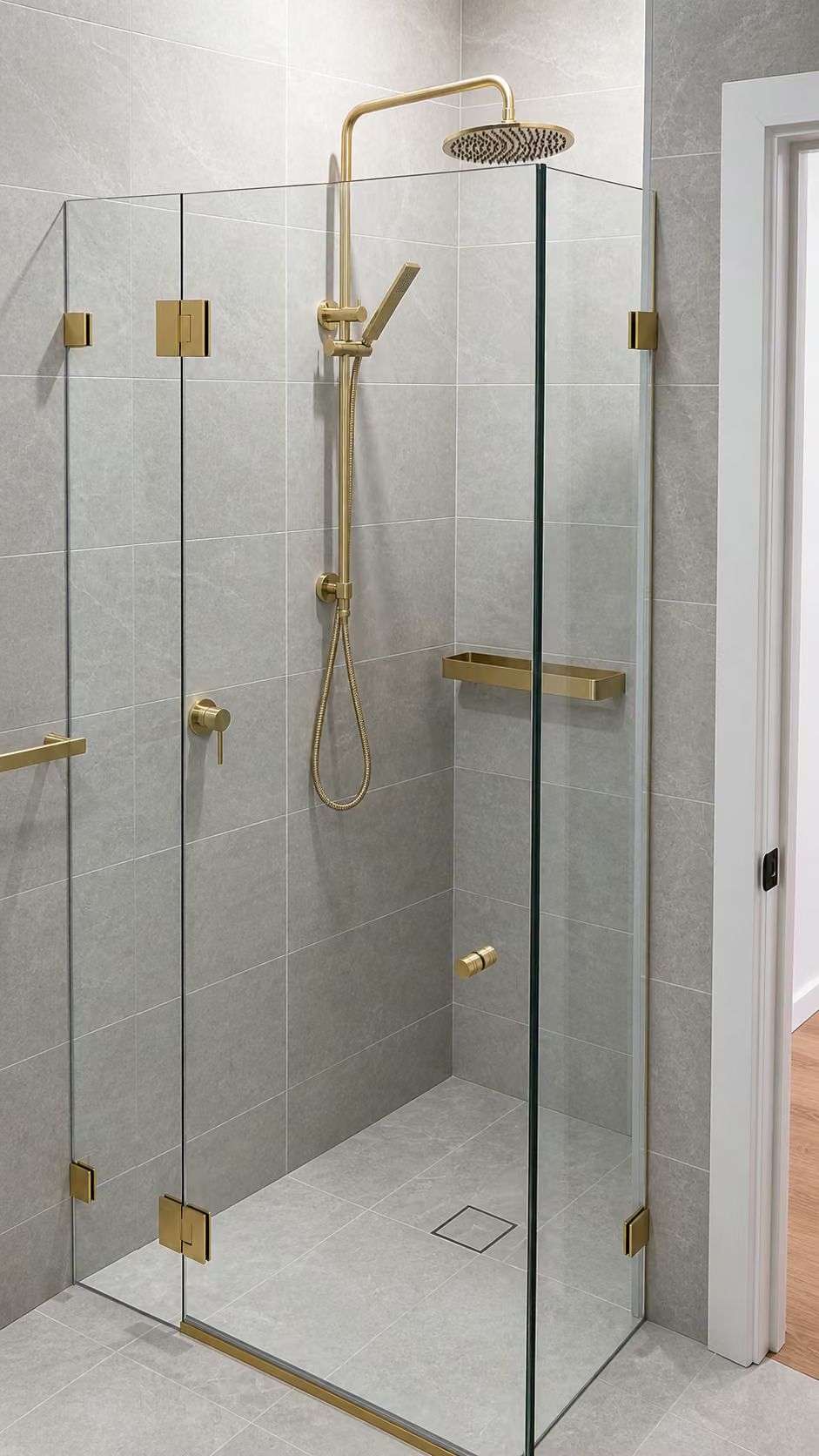Glass walk-in shower with gold fixtures and gray tiled walls in a bathroom