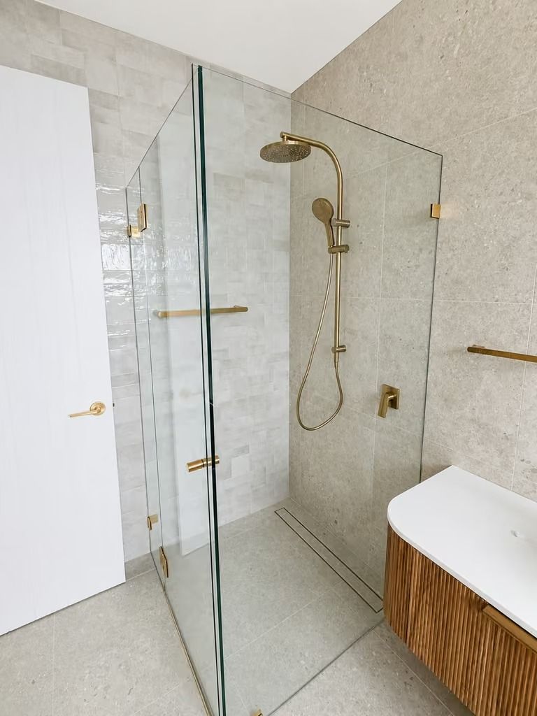 Modern bathroom shower with glass enclosure, brass fixtures, and white tiled walls