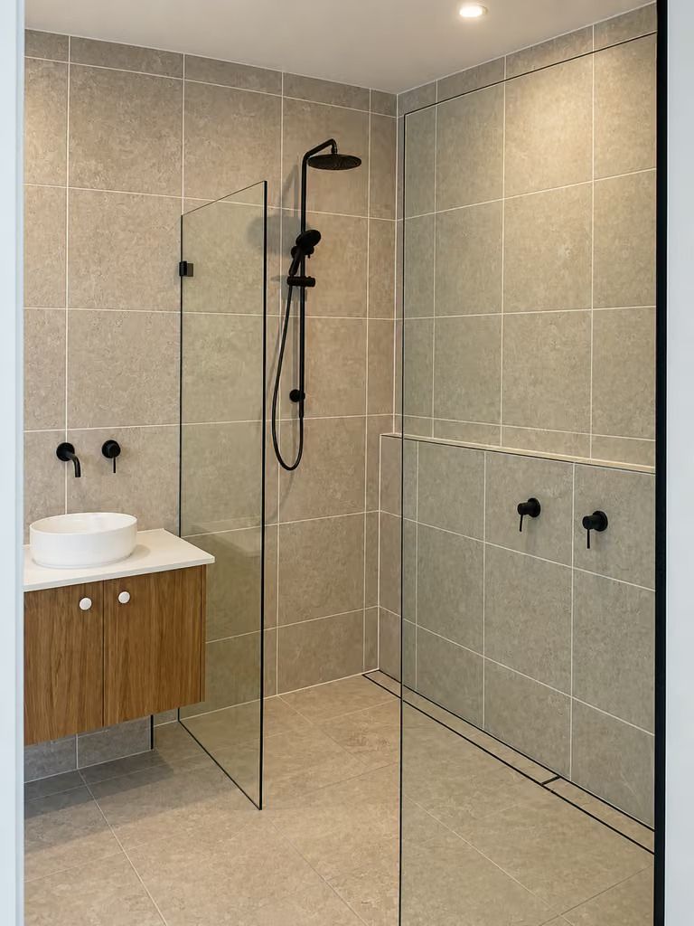 Modern beige tiled bathroom with glass shower, black fixtures, and wood vanity.