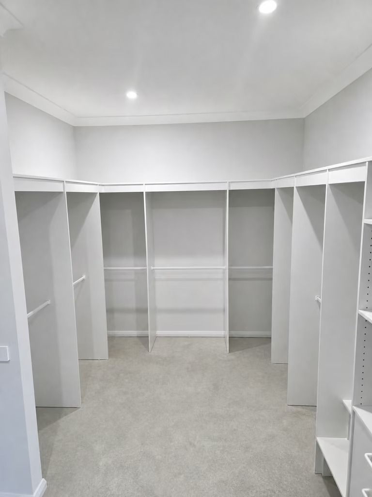 Empty white walk-in closet with built-in shelving and hanging rods on beige carpet.