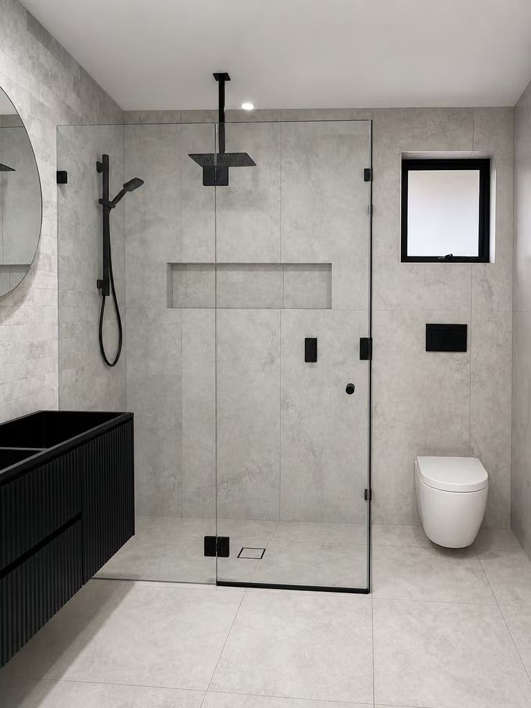 Modern black-and-white bathroom with walk-in shower, toilet, and window.