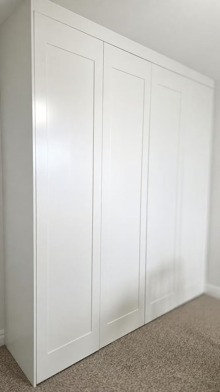 White built-in closet with three doors against a white wall and beige carpet.