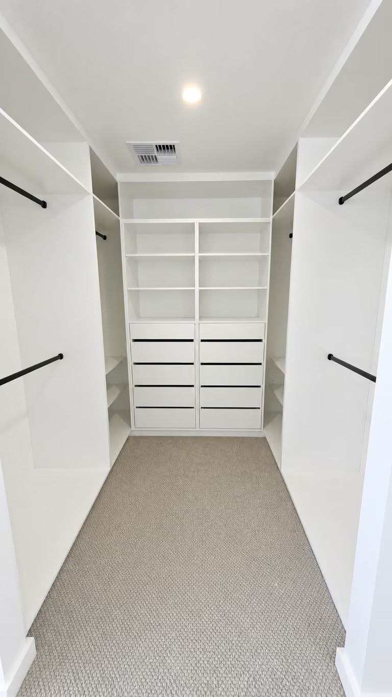 White walk-in closet with built-in shelves, drawers, and hanging rods on both sides.