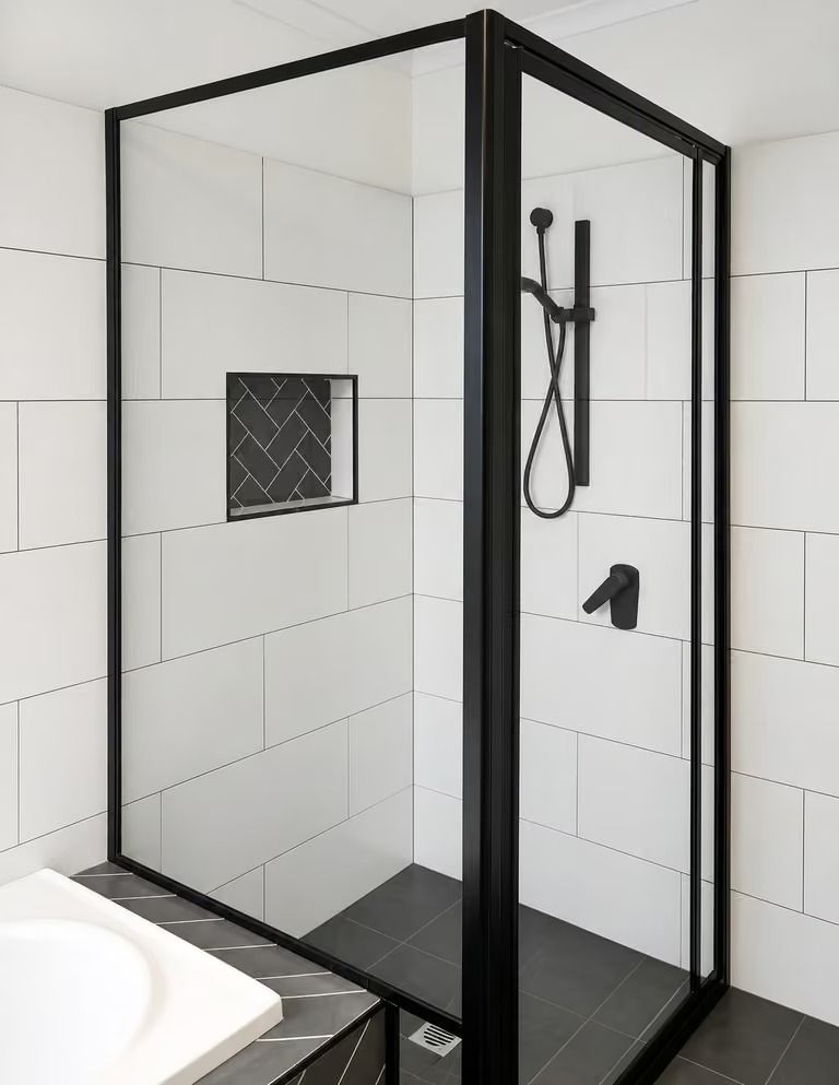 Black-framed glass walk-in shower with white tiled walls and black fixtures in a modern bathroom