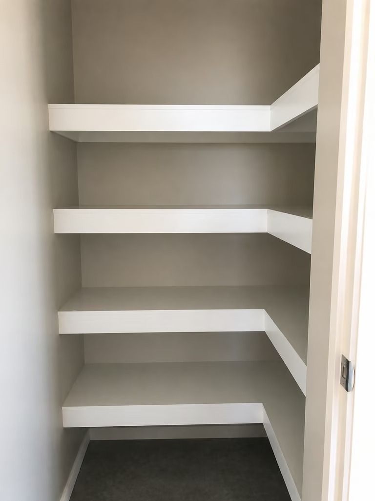Empty built-in closet with white shelves and gray walls