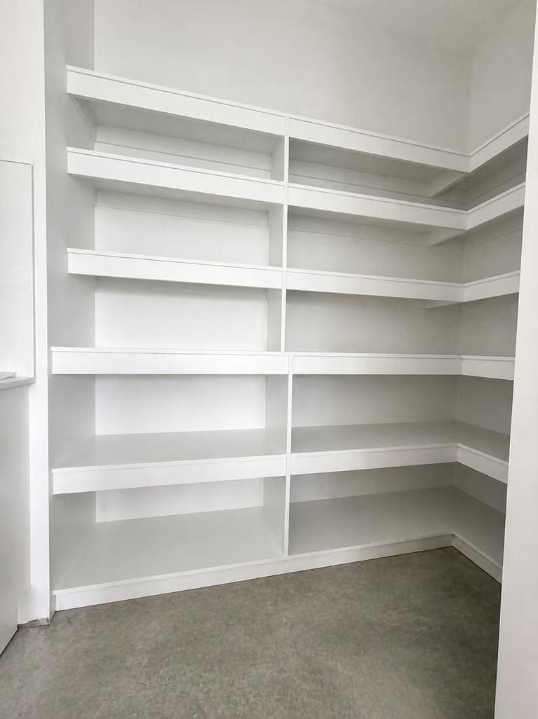 Empty white built-in shelving in a carpeted closet or storage room.