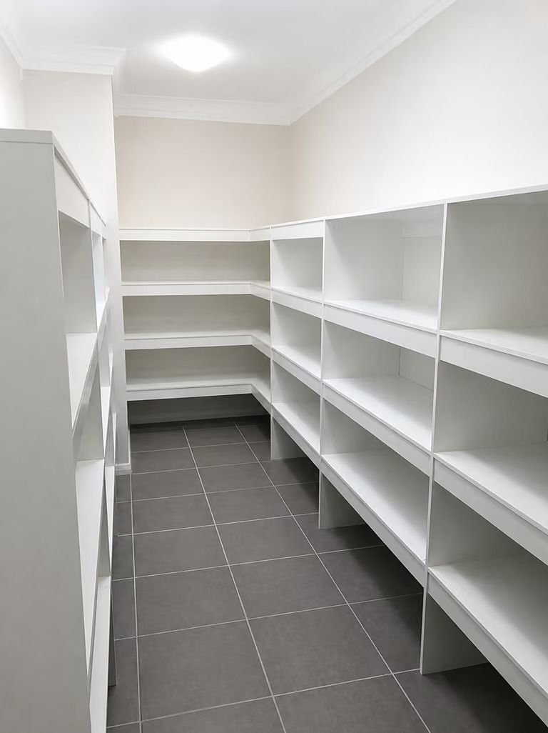 Empty white pantry with built-in shelves and gray tiled floor.