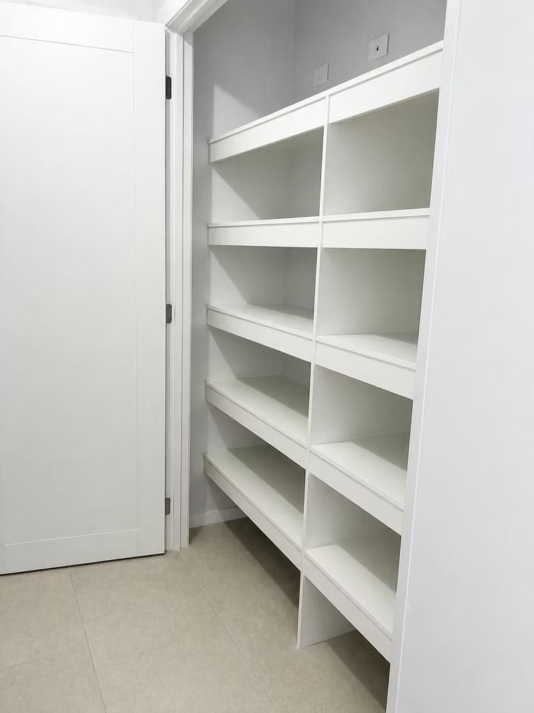 Empty white pantry with built-in shelves and a closed door