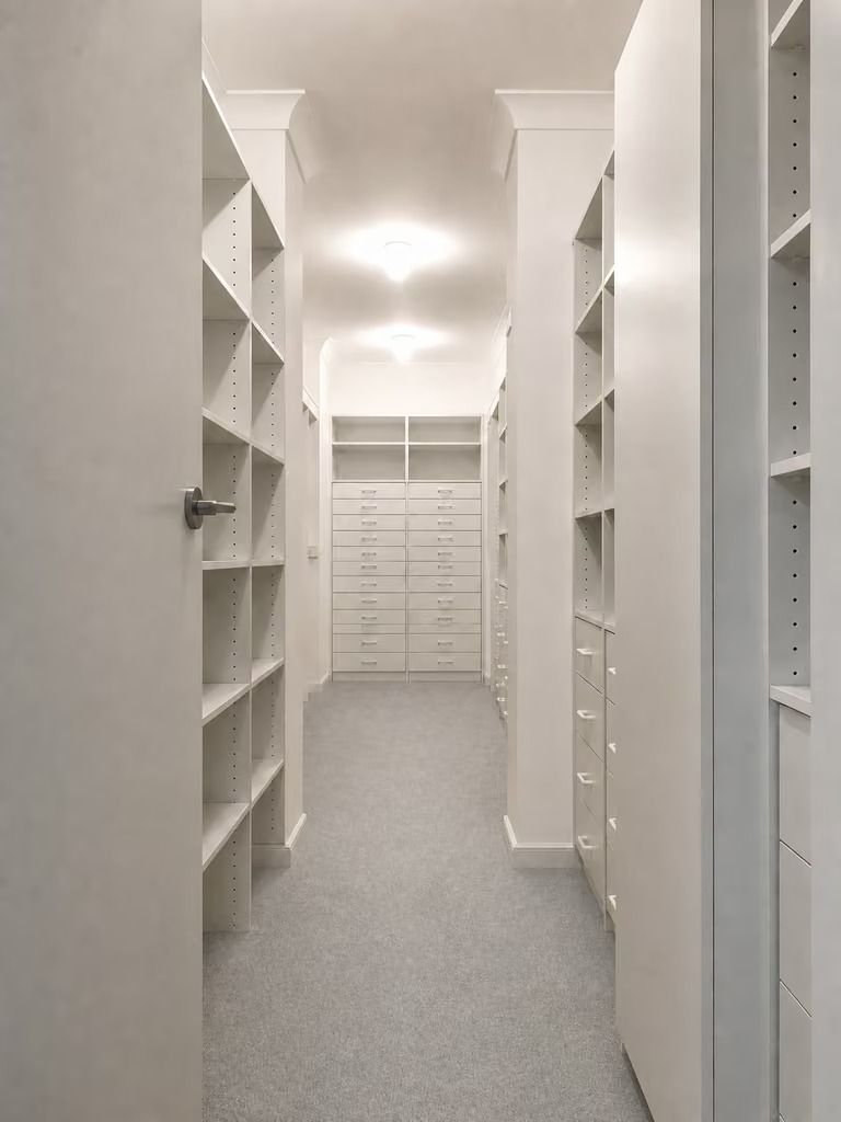 Bright walk-in closet with white shelves and drawers on both sides and a gray carpeted floor.