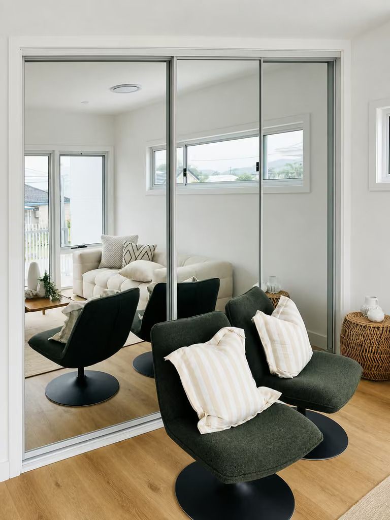 Modern living room with dark lounge chair, striped pillows, large mirrored closet doors, and wood floors