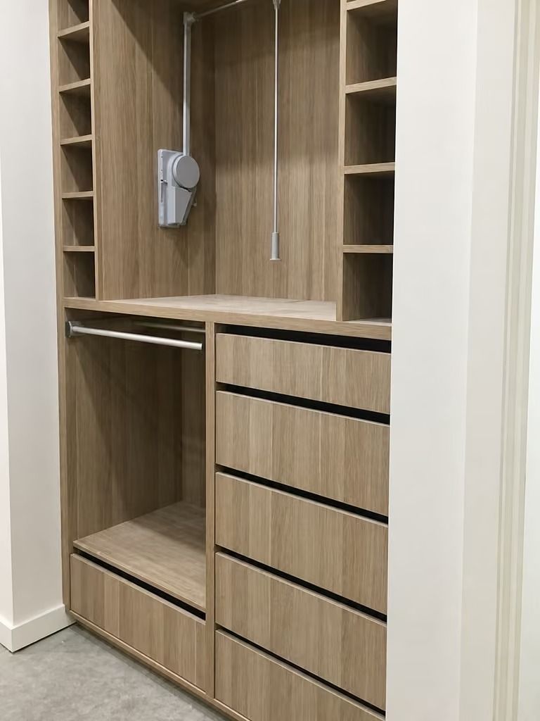 Wooden closet with open shelves, hanging rod, and drawers in a minimalist room.
