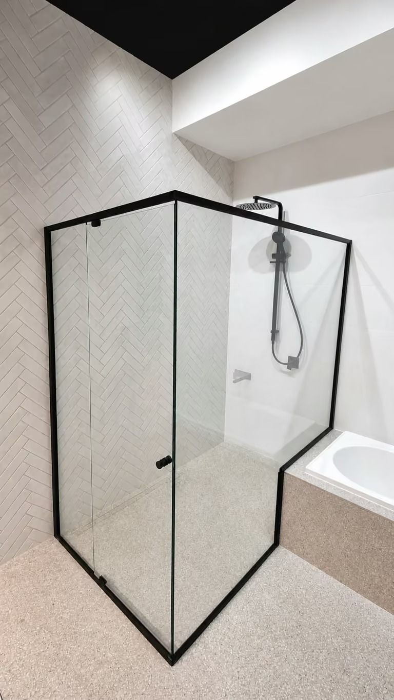 Glass-enclosed shower with black frame beside a white bathtub in a modern bathroom
