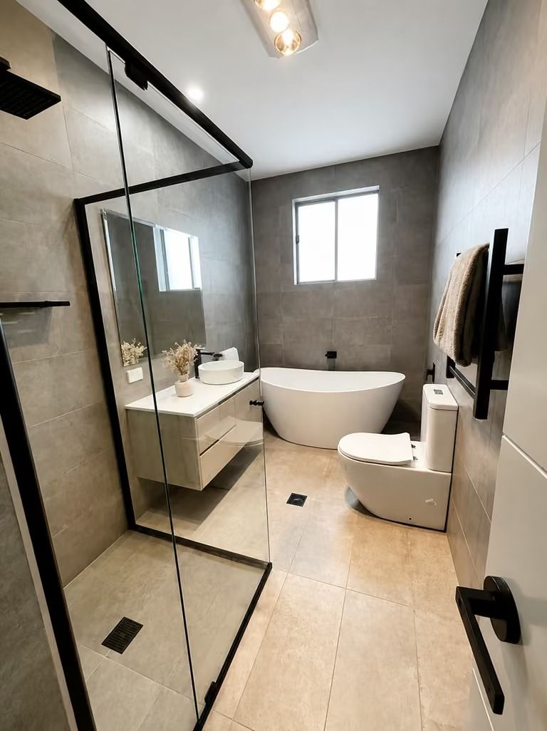 Modern bathroom with glass shower, vanity, freestanding tub, toilet, and window