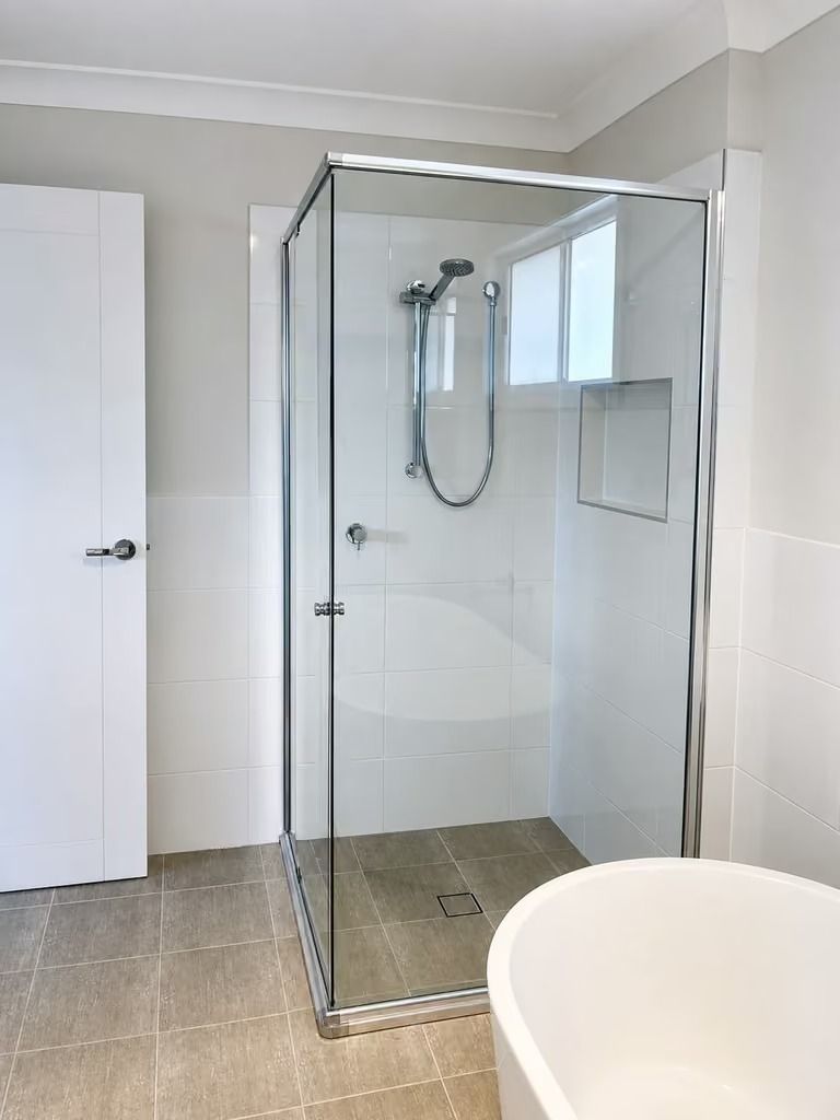 Modern bathroom with glass shower enclosure, white walls, tiled floor, and a partially visible toilet.