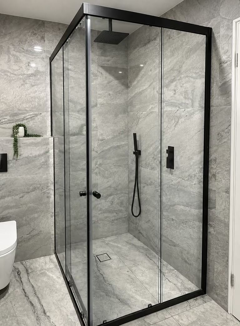 Modern walk-in shower with black-framed glass enclosure in a marble-tiled bathroom