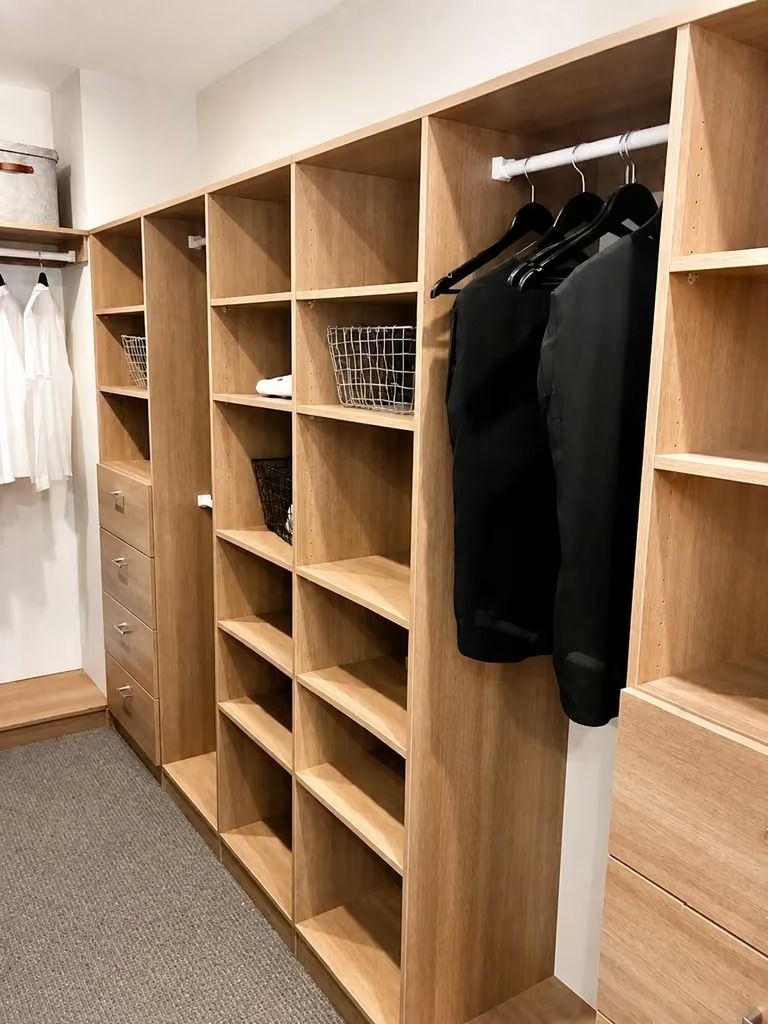 Wooden wardrobe cubbies with hanging black clothes in a minimalist dressing room