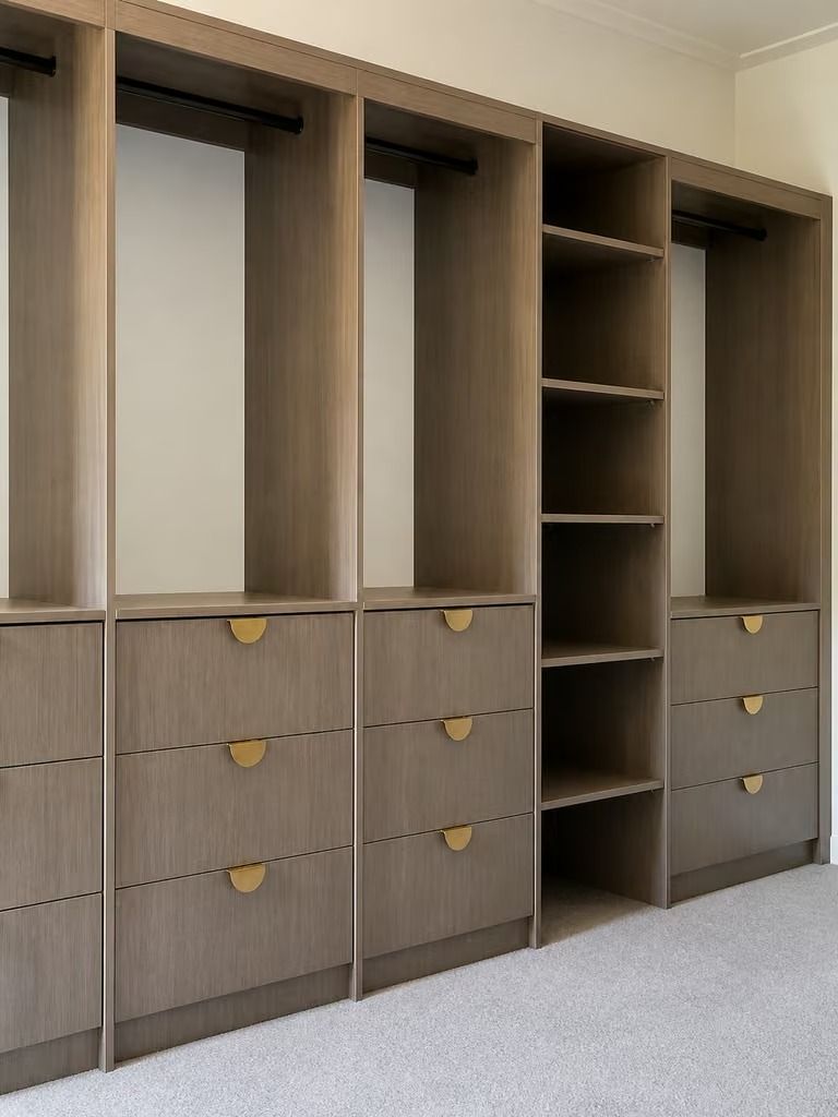 Built-in wooden wardrobe with open shelves and drawers in a beige bedroom