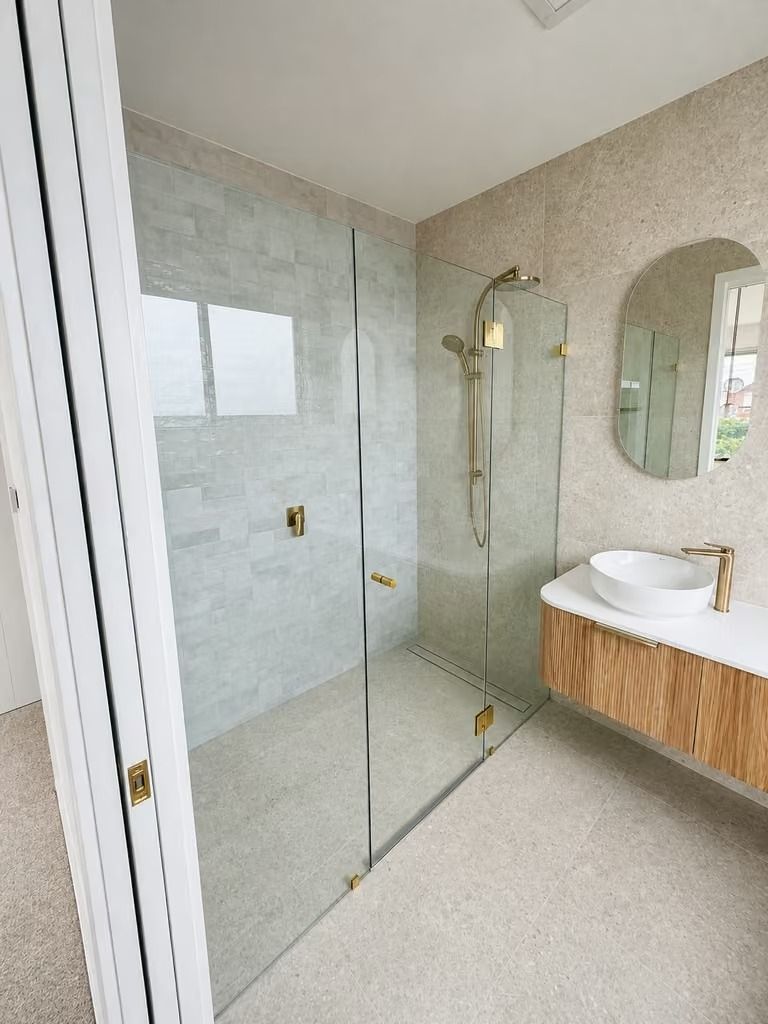 Modern bathroom with glass shower, gold fixtures, floating wood vanity, and oval mirror