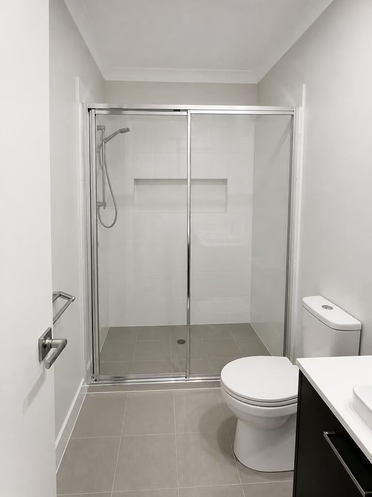 Modern bathroom with a glass shower, toilet, and sink on light gray tile.