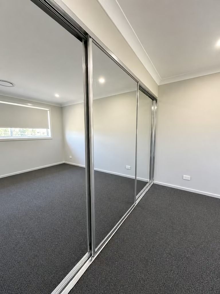 Empty room with mirrored closet doors, gray carpet, and a small window.