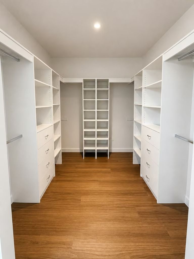 Empty white walk-in closet with built-in shelves and drawers, wood floor, and a central organizer unit
