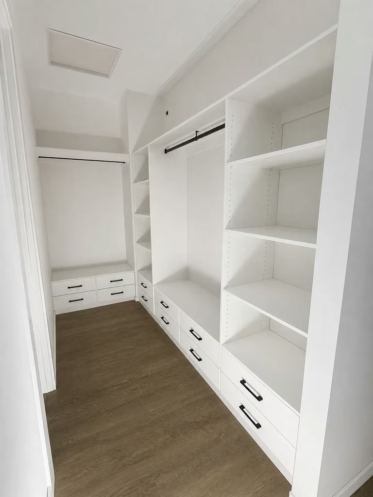 Empty white walk-in closet with shelves, hanging rods, and drawers, plus dark wood flooring.