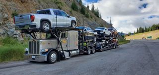 Car hauler trailer loaded with vehicles on a mountain road under a cloudy sky