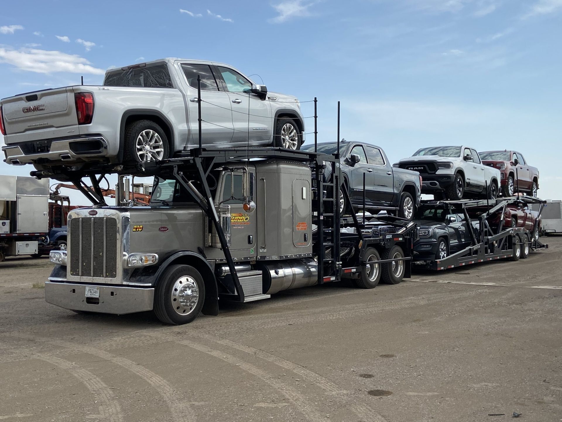 Car carrier truck loaded with several pickup trucks in an outdoor lot under a blue sky