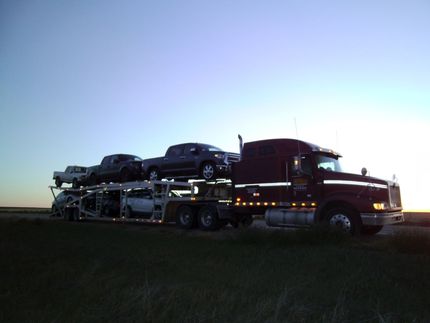 Flatbed truck carrying multiple cars at dusk on a rural road