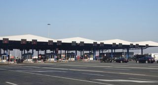 Wide toll plaza with multiple lanes, cars, and red-lit signs under a clear blue sky
