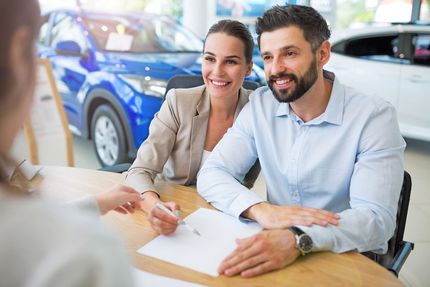 Smiling couple signing papers with a salesperson at a car dealership
