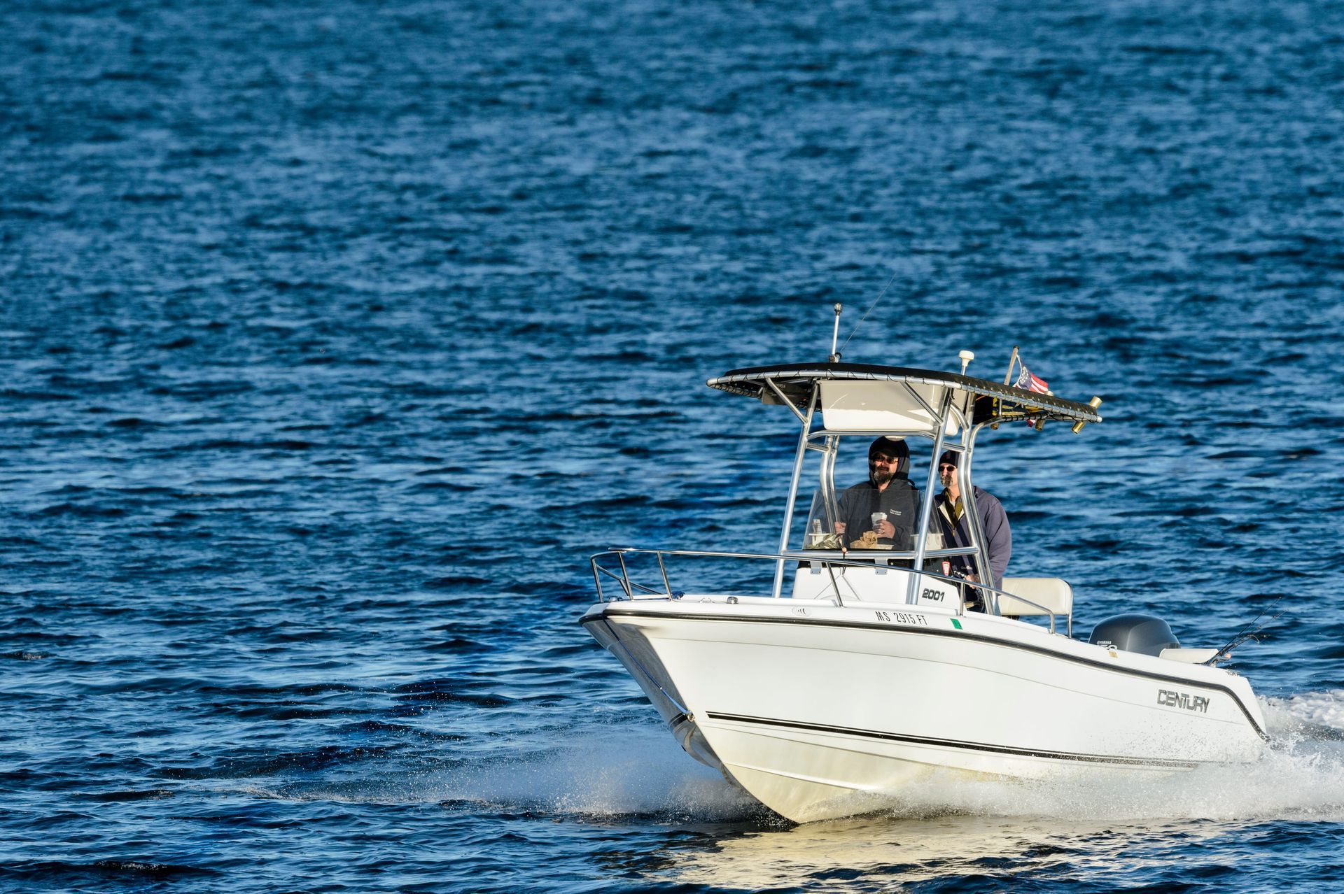 White motorboat speeding across blue water with spray from the bow