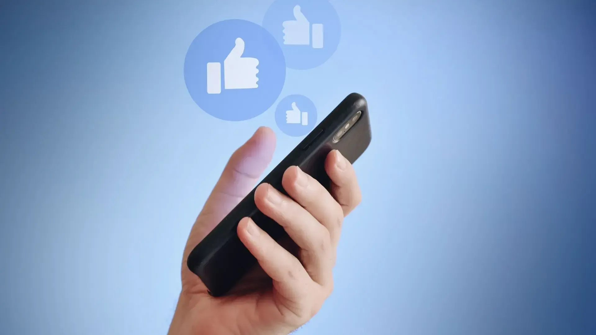 A person is holding a cell phone with thumbs up icons coming out of it.