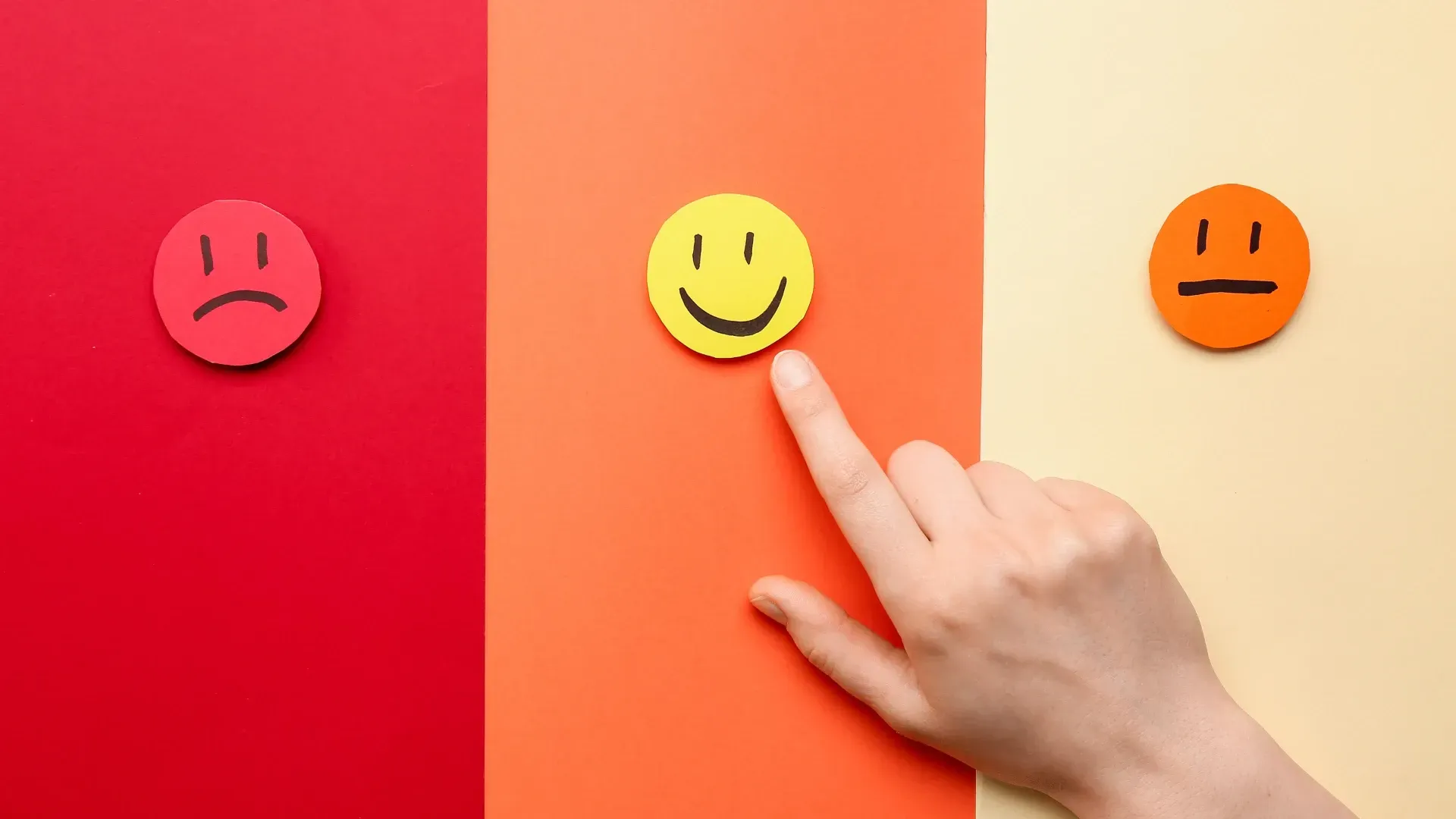 A person is pointing at a smiley face on a red , orange and yellow background.