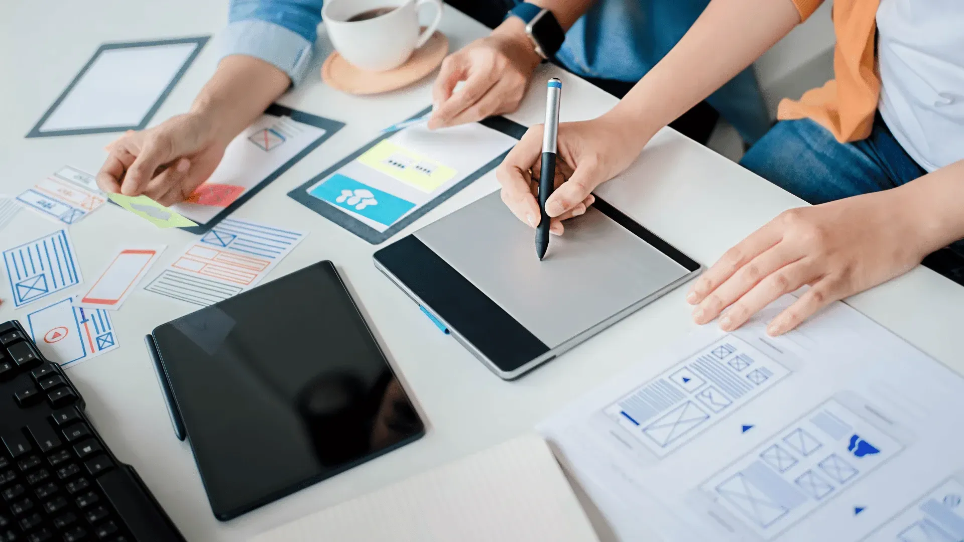 Two people are sitting at a table using a tablet and a pen.