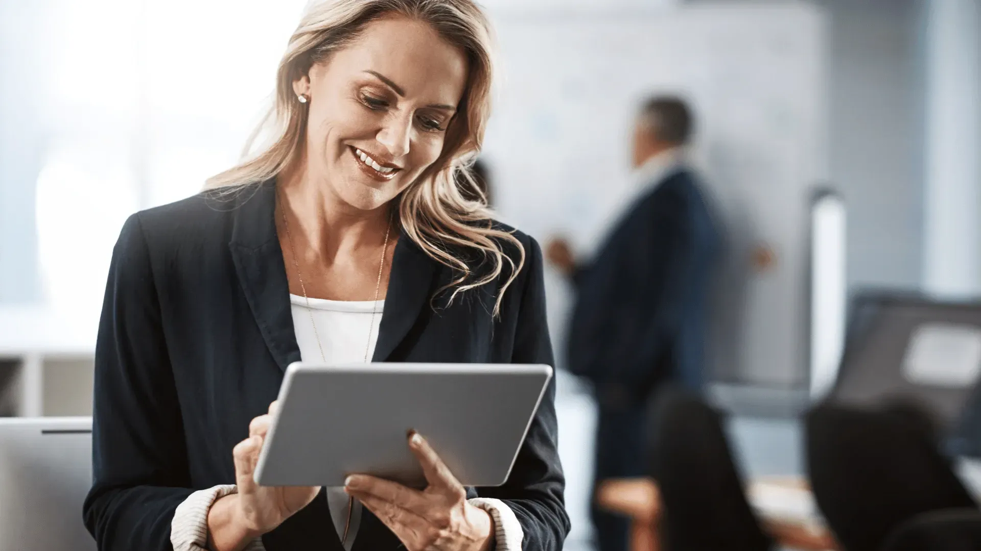 A woman is holding a tablet in her hands and smiling.