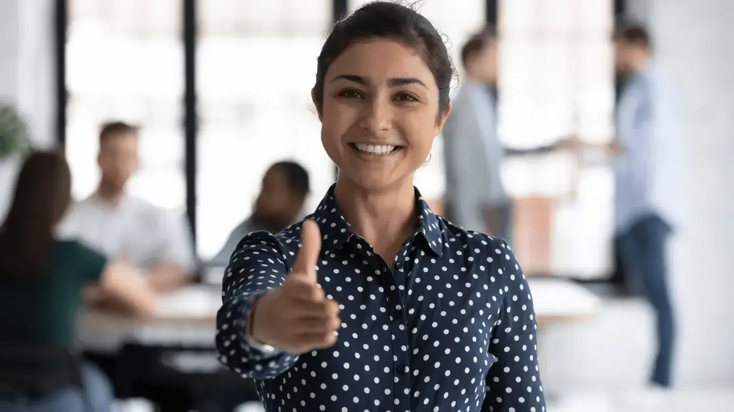 A woman is giving a thumbs up sign in an office.