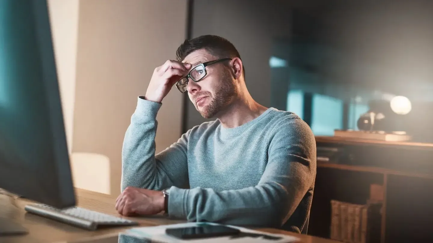 A man wearing glasses is sitting at a desk in front of a computer.