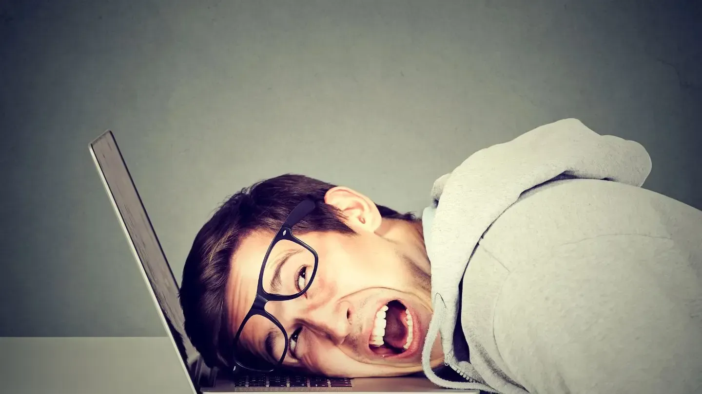 A man with glasses is laying on top of a laptop computer.
